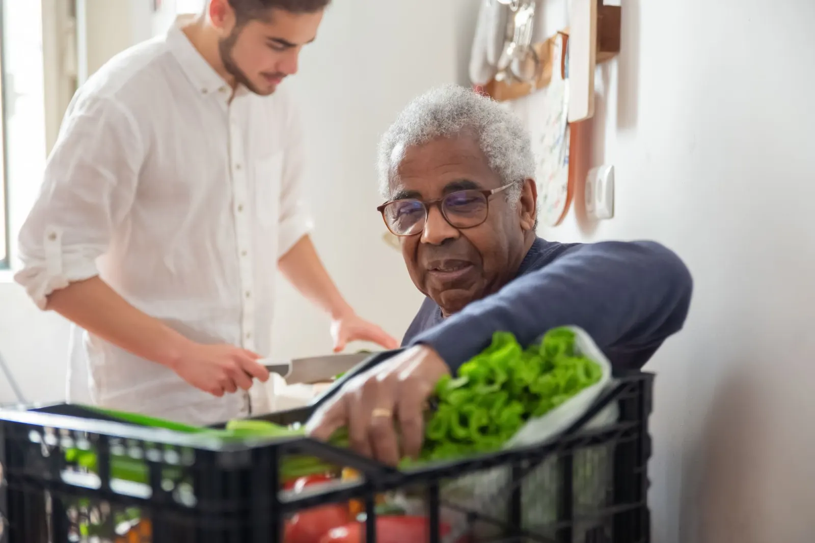 Zorgverlener en oudere man ruimen samen de boodschappen op