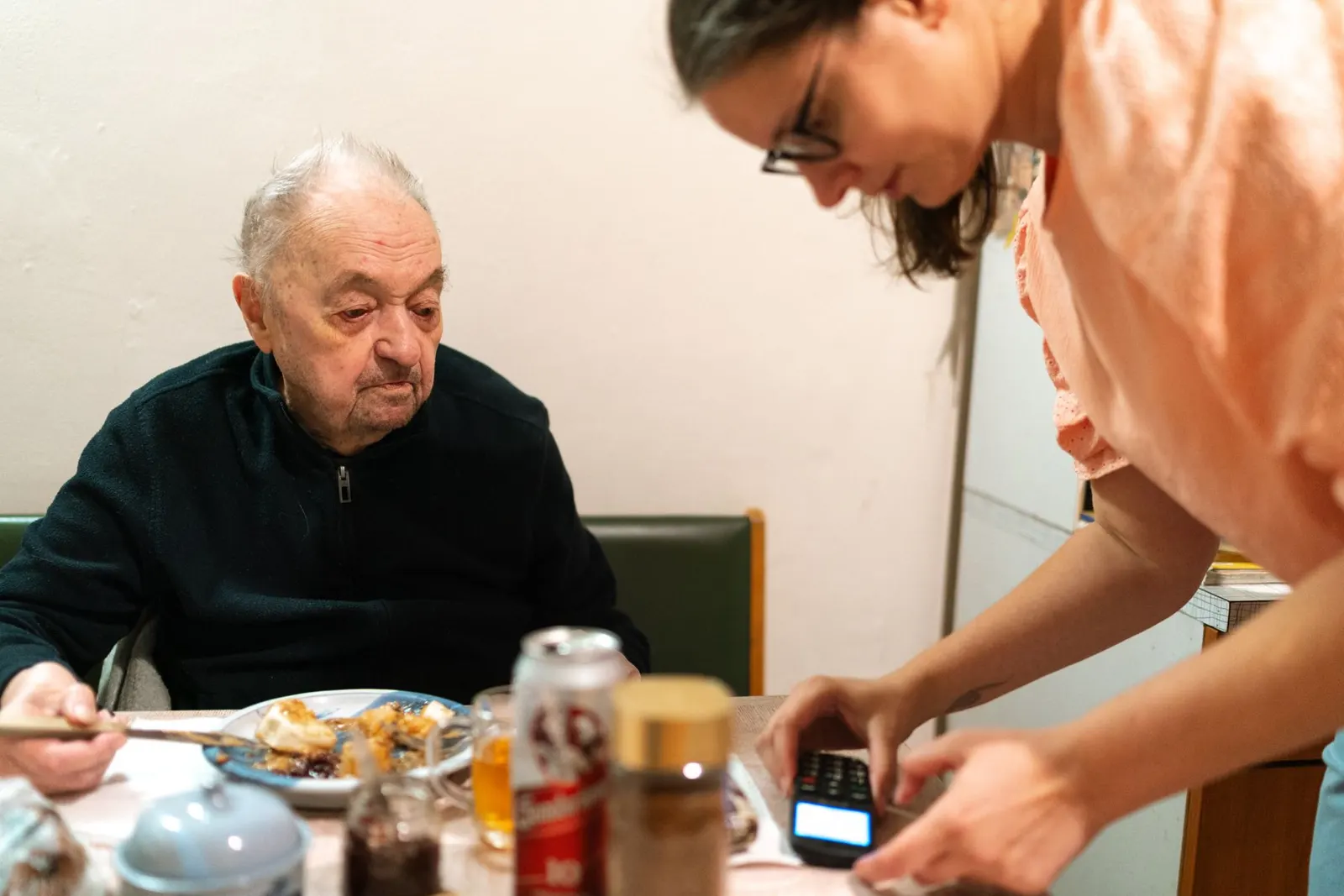 Zorgverlener helpt een oudere man aan tafel bij de maaltijd