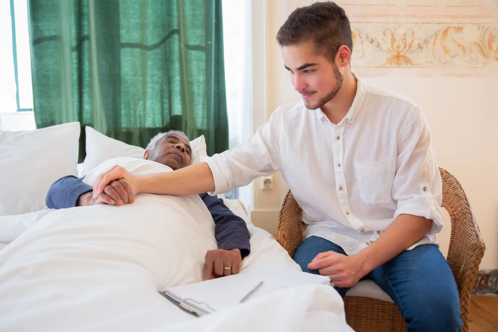 Zorgverlener zit naast een oudere man in bed en houdt zijn hand vast